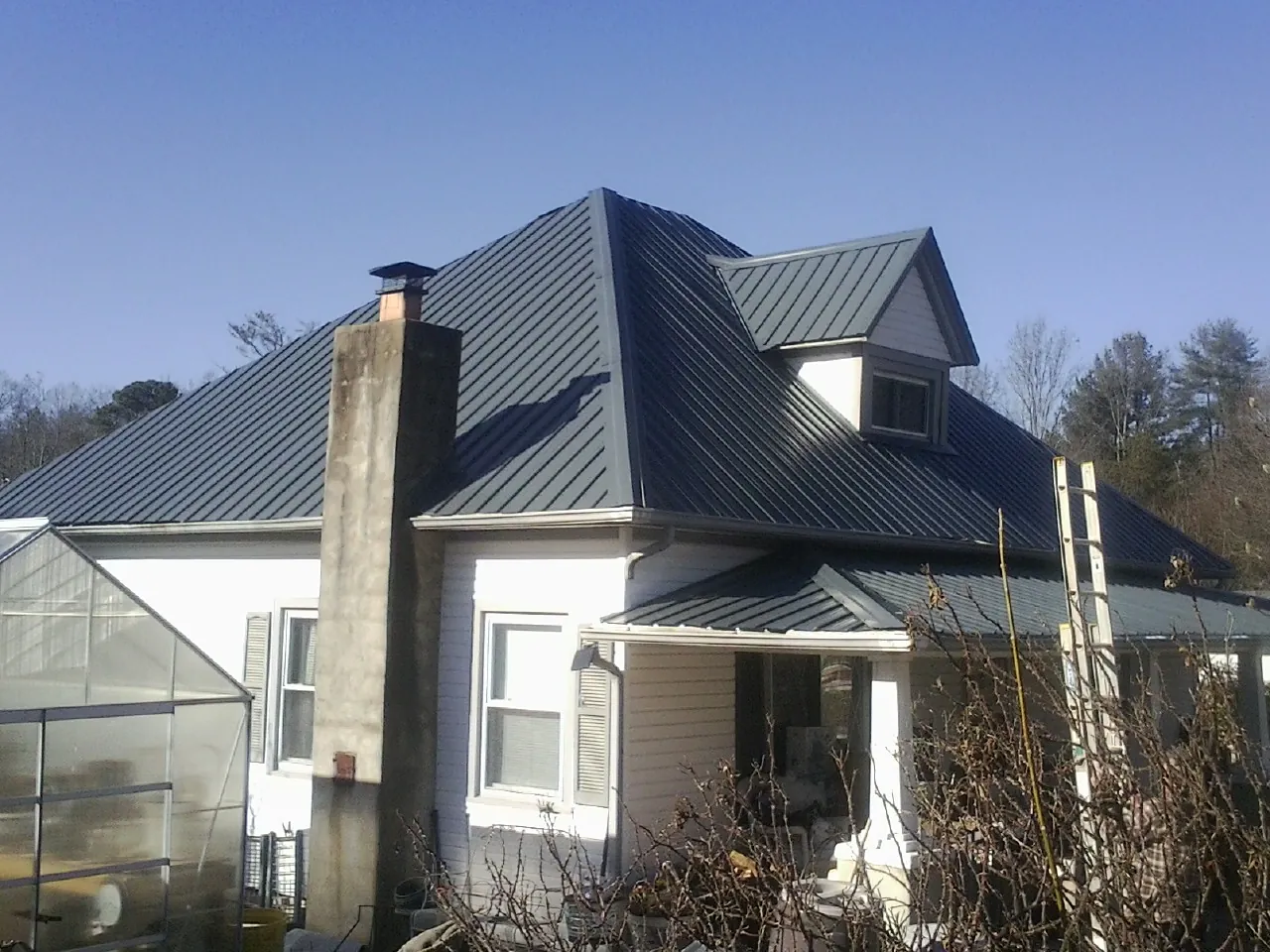 Dark blue standing seam metal roof on a white farmhouse with dormer — Slate & Tile Roof Repair by Roofing Brothers in Efland