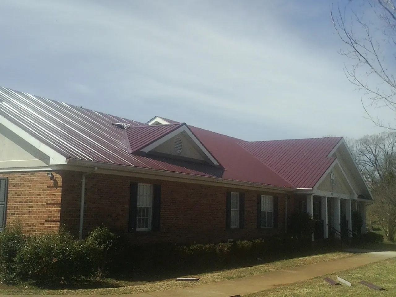 Red metal roof with gabled entries on a long brick building, from a Hail Damage Roof Repair job in Efland
