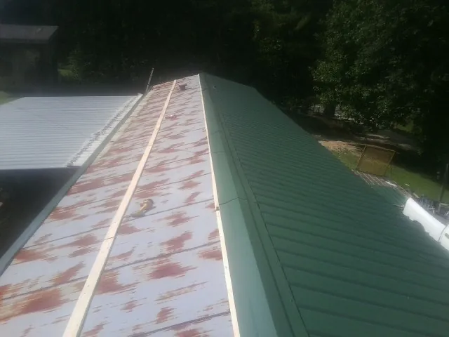 Old rusted panels beside newly installed green metal roofing — Wind Damage Roof Repair by Roofing Brothers in Efland