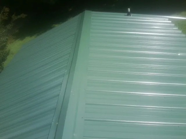 New green metal panels meeting at the ridge of a roof — Flat Roof Repair work by our crew in Efland