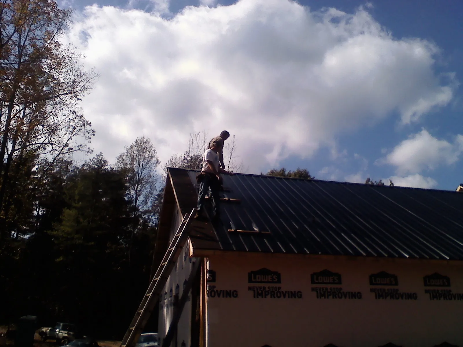Roofer fastening dark metal panels high against a cloudy sky, from a Roof Inspection job in Efland