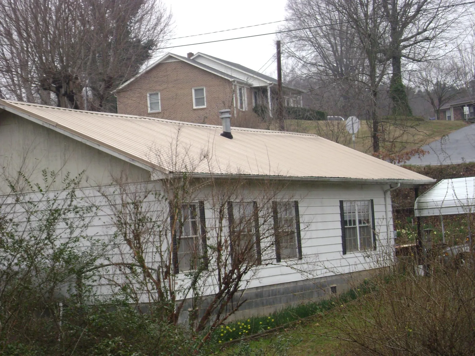 Tan metal roof on a white sided house set into a hillside — Commercial Roofing by Roofing Brothers in Efland