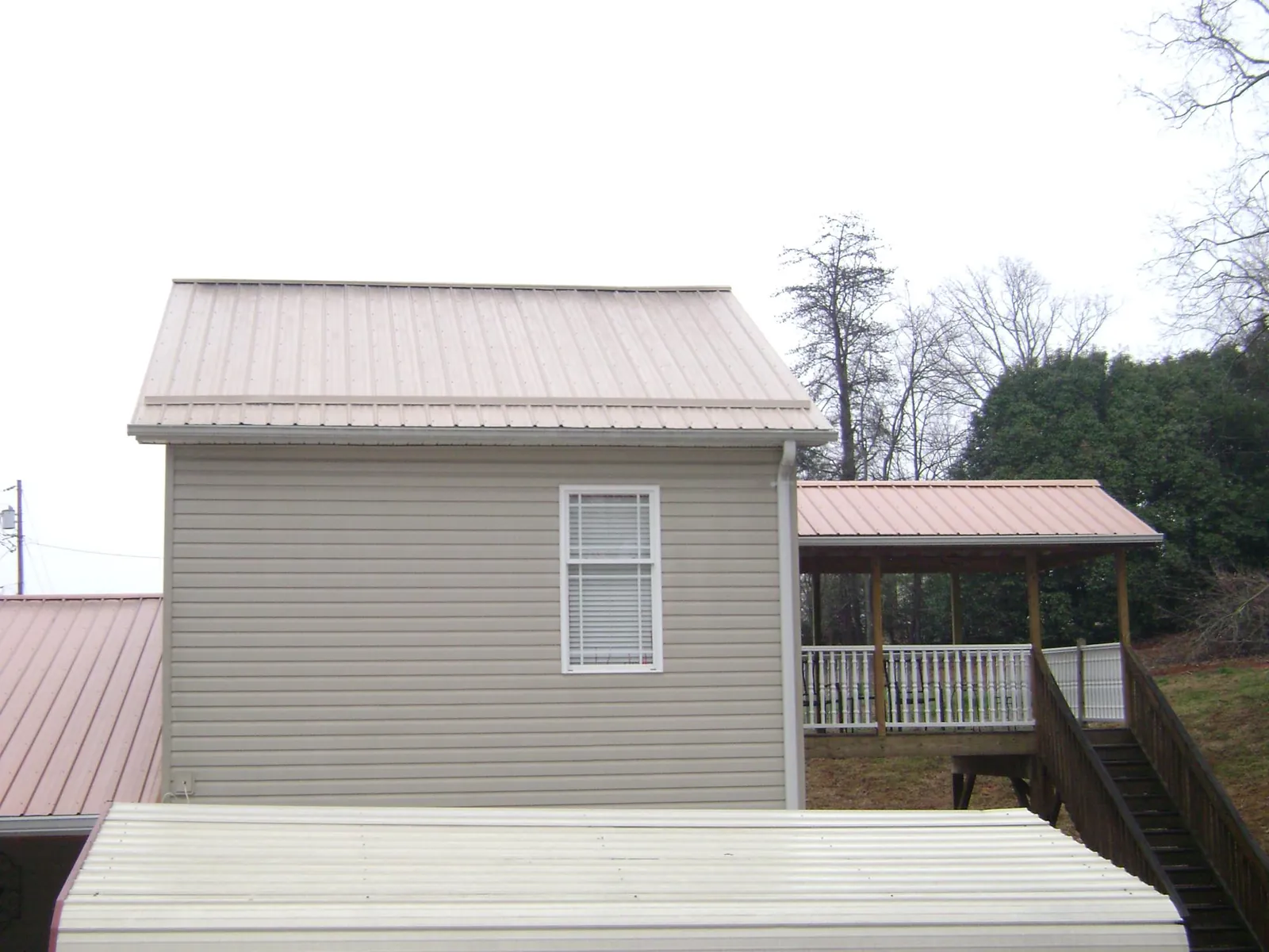 Tan metal roofs on a two story addition and attached porch, from a Roof Replacement job in Efland